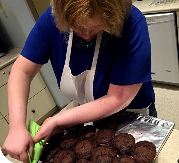 Person applying icing to muffins on a tray