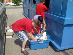 Youth loading paper recycling into a large metal recycling bin
